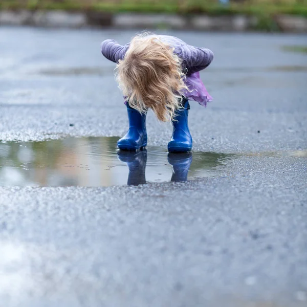 Μικρό χαρούμενο κορίτσι τρέχει μέσα από τις λιμνούλες σε λαστιχένιες μπότες, — Φωτογραφία Αρχείου