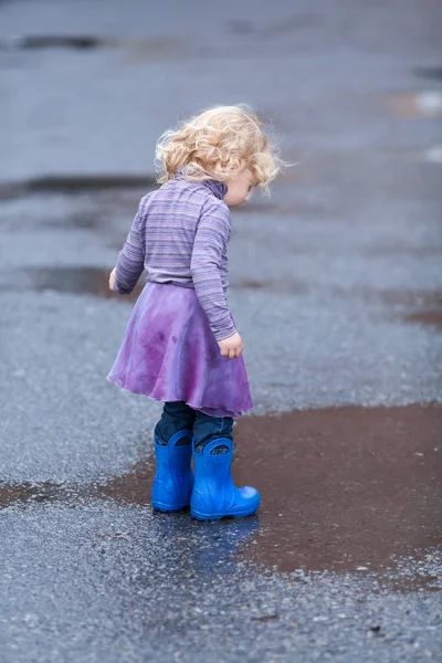 Kleines fröhliches Mädchen läuft in Gummistiefeln durch die Pfützen, — Stockfoto