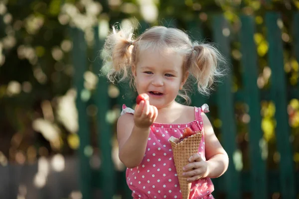 Glückliches kleines Mädchen isst Beeren im Sommer Garten, im Freien. — Stockfoto