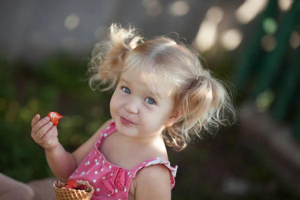 Feliz niña está comiendo bayas en el jardín de verano, al aire libre . — Foto de Stock