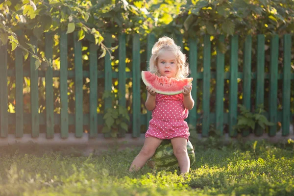 Mutlu küçük kız yaz bahçesinde karpuz yiyor, açık.