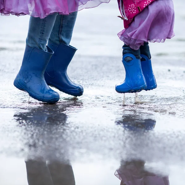 Mutter und Tochter springen in blauen Gummistiefeln in eine Pfütze, — Stockfoto