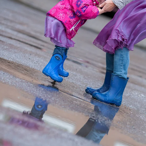 Moeder en dochter springen in een plas in blauwe rubberen laarzen, — Stockfoto