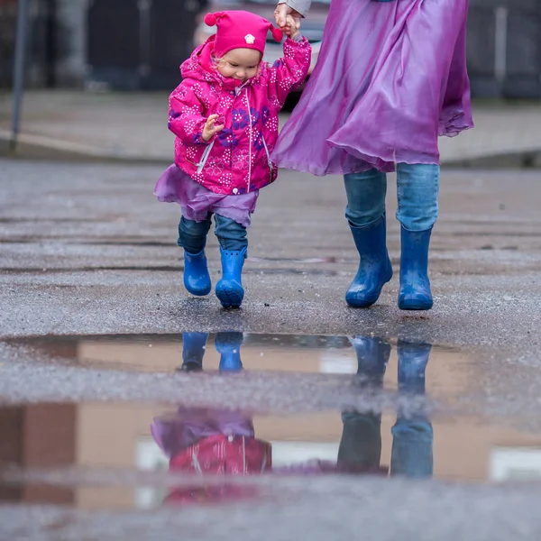 Mutter und Tochter springen in blauen Gummistiefeln in eine Pfütze, — Stockfoto