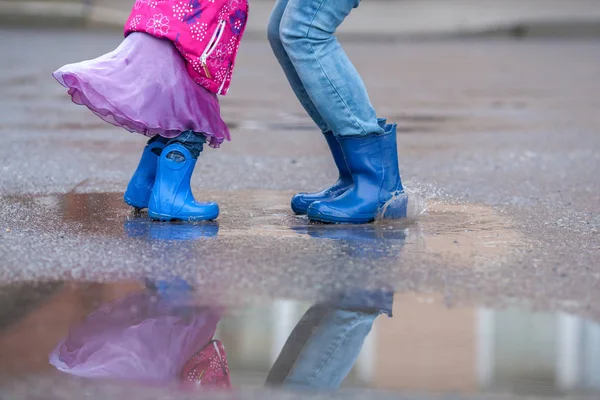 Mutter und Tochter springen in blauen Gummistiefeln in eine Pfütze, — Stockfoto