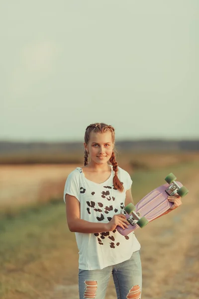 Молодая счастливая милая девушка ездит на скейтборде по дороге, на открытом воздухе — стоковое фото
