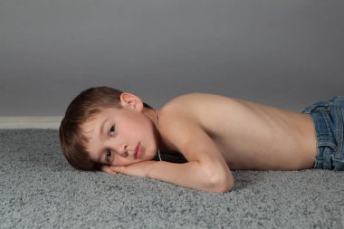 Gri halıda yerde yatan üzgün çocuğun portresi