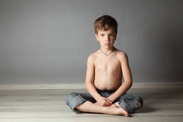 Retrato de menino bonito sentado no chão contra uma parede cinza — Fotografia de Stock