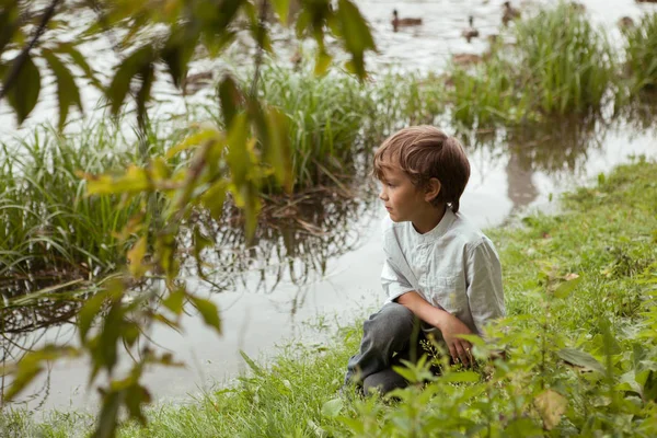 Der Junge sitzt in der Nähe des Flusses im Sommerpark — Stockfoto