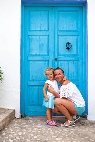 Family vacation in Europe. Mother and daughter at street of typical spain traditional village. Woman and child near the old blue door