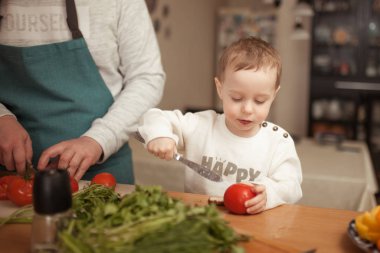 Küçük bir çocuk babasının mutfakta yemek pişirmesine yardım ediyor.