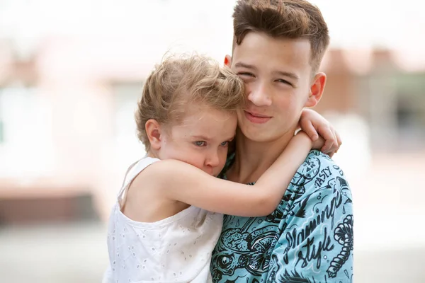 Jüngere hübsche Schwester umarmt ihren älteren Bruder, Porträt eines Mädchens und Teenagers vor dem Hintergrund der Stadt. — Stockfoto