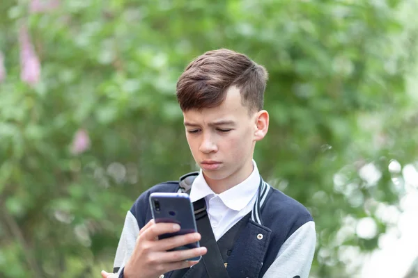 The student looks into the phone on the background of a green park — Stock Photo, Image