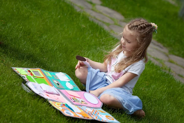 Meisje zit op een groene weide en speelt met een pop — Stockfoto
