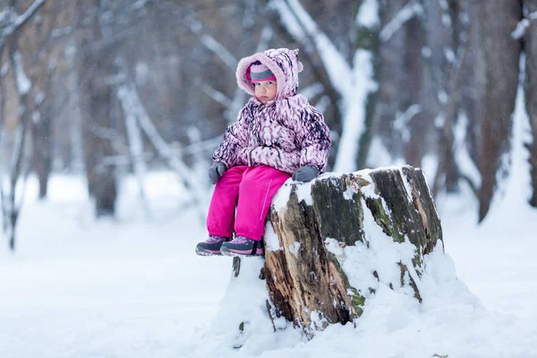 Pokovená dívka sedící na pahýlu v zimním parku — Stock fotografie
