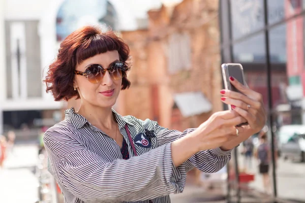 Nette Frau, die an einem sonnigen Sommertag auf der Straße läuft und ein Smartphone benutzt — Stockfoto