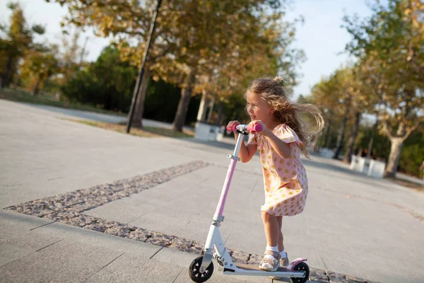 Glückliches hübsches Mädchen fährt einen Motorroller in einem schönen Herbstpark — Stockfoto