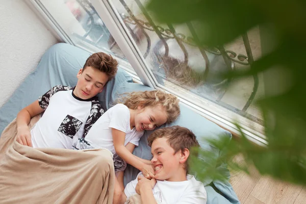 小さな女の子と兄は窓の近くのソファの上に横たわっている 子供たちは笑って話している — ストック写真