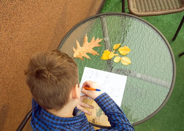 少年は 何かを書いています 少年は 屋外の宿題をやっています 少年は紙の上に描画または手紙を書いて — ストック写真