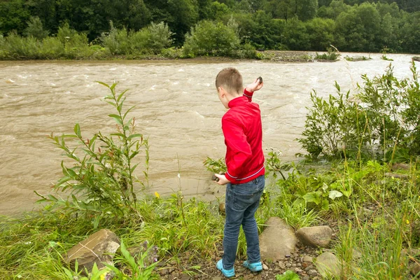 Little boy throwing stones in the water. Boy in red jacket throw rocks