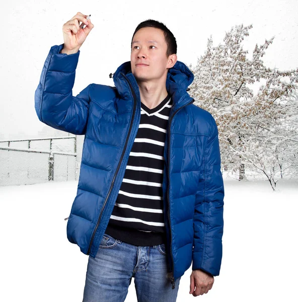 亚洲人在蓝色下来软垫外套 反对雪冬天背景 户外的男人穿着暖和的冬衣 在透明的木板上写着一些东西 雪和冷 — 图库照片