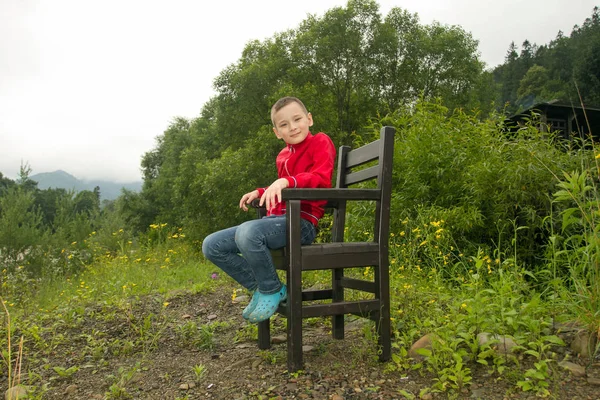 Pojken sitter på stol i skogen — Stockfoto