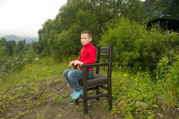 Chłopiec siedzi na krześle w lesie — Zdjęcie stockowe