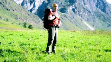 Sırt çantası ile yeşil dağ çayır üzerinde yürüyen adam hiking. Yaz spor ve eğlence kavramı.