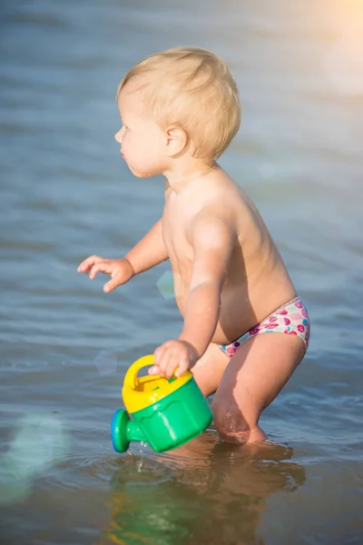 Lindo bebé jugando en la playa de arena y en agua de mar . — Foto de Stock