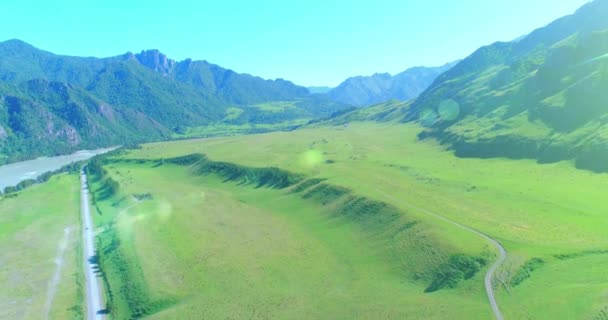 Aerial rural mountain road and meadow at sunny summer morning. Asphalt highway and river. — Stock Video
