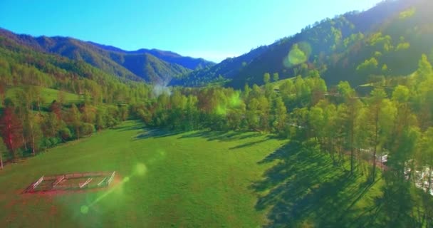 Mid air flight over fresh mountain river and meadow at sunny summer morning. Rural dirt road below. — Stock Video