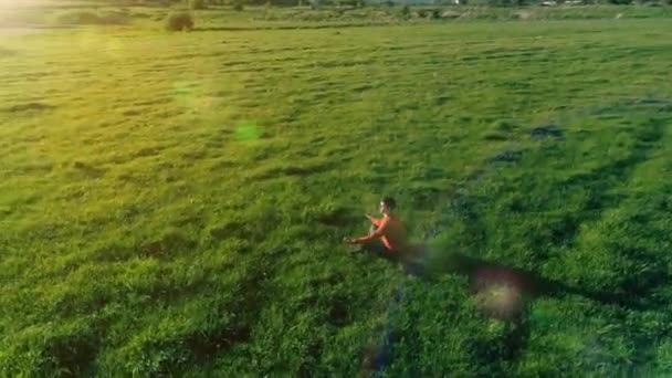 Låg höjd radiell flygning över sport yoga man på perfekt grönt gräs. Solnedgång i bergen. — Stockvideo