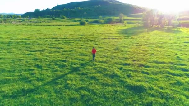 完璧な緑の芝生の牧草地でスポーツマンの上を飛行します。山の夕日 — ストック動画