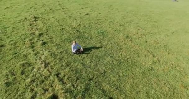 UHD 4k вигляд з повітря. Низький орбітальний політ над бізнесменом, що сидить на зеленій траві з блокнотом на полі — стокове відео