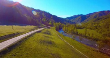 Güneşli yaz sabahında taze dağ nehri ve çayır üzerinde uçuşun ortasında. Aşağıdaki kırsal toprak yol.