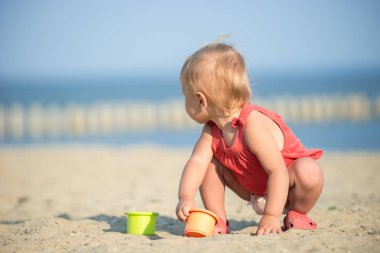 Denize yakın kumlu plajda oynayan Kırmızı elbiseli kız bebek. 