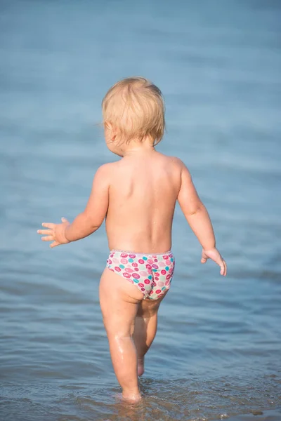 Bebê bonito brincando na praia e na água do mar . — Fotografia de Stock