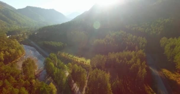 Vôo a meio do ar sobre o rio e o prado frescos da montanha na manhã ensolarada do verão. Estrada de terra rural abaixo. — Vídeo de Stock