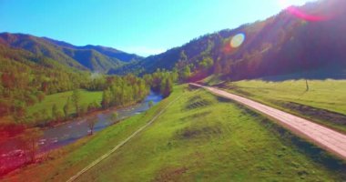 Güneşli yaz sabahında taze dağ nehri ve çayır üzerinde uçuşun ortasında. Aşağıdaki kırsal toprak yol.