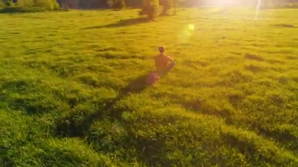 Penerbangan ketinggian rendah radial di atas olahraga pria yoga di rumput hijau yang sempurna. Matahari terbenam di gunung. — Stok Video
