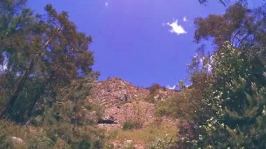 Yazın 4K UHD dağ zaman dilimi. Bulutlar yeşil ağaçları ve güneş ışınlarını hareket ettirir.