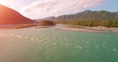 4k UHD hava görüntüsü. Güneşli yaz sabahında taze soğuk dağ nehri üzerinde alçak uçuş. Horisont 'ta yeşil ağaçlar ve güneş ışınları