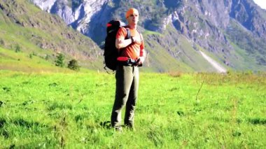 Sırt çantası ile yeşil dağ çayır üzerinde yürüyen adam hiking. Yaz spor ve eğlence kavramı.