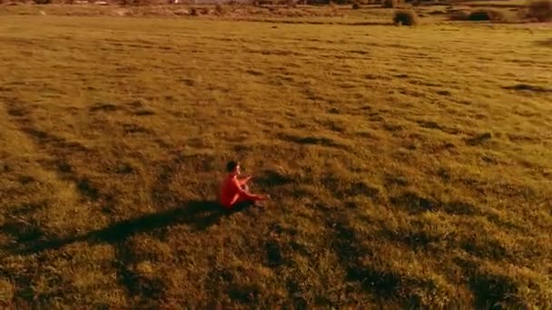 Vuelo radial de baja altitud sobre el hombre del yoga del deporte en hierba verde perfecta. Puesta de sol en montaña. — Vídeos de Stock