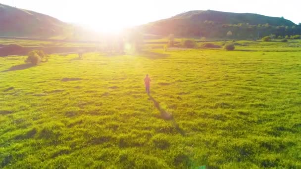 Vuelo sobre el hombre del deporte en el prado de hierba verde perfecto. Puesta de sol en montaña — Vídeos de Stock