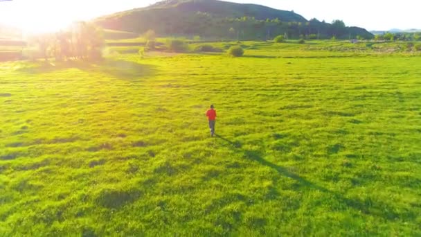 Flight over sport man at perfect green grass meadow. Sunset in mountain — Stock Video