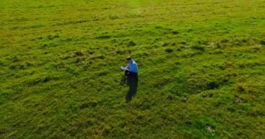 UHD 4k havadan görünümü. Defter pad ile yeşil çim sahasında oturan işadamı üzerinde düşük yörünge uçuş