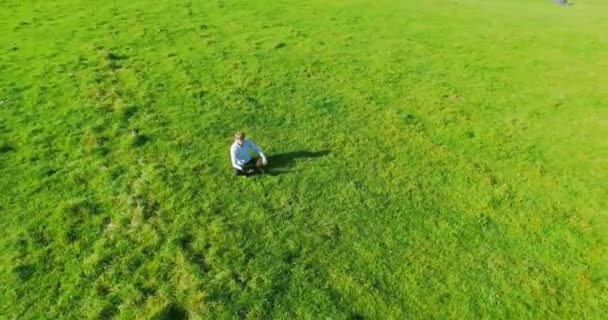 UHD 4k vista aérea. Vuelo orbital bajo sobre hombre de negocios sentado sobre hierba verde con bloc de notas en el campo — Vídeo de stock