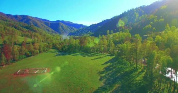 Mid air flight over fresh mountain river and meadow at sunny summer morning. Rural dirt road below. — Stock Video