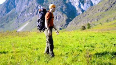 Sırt çantası ile yeşil dağ çayır üzerinde yürüyen adam hiking. Yaz spor ve eğlence kavramı.